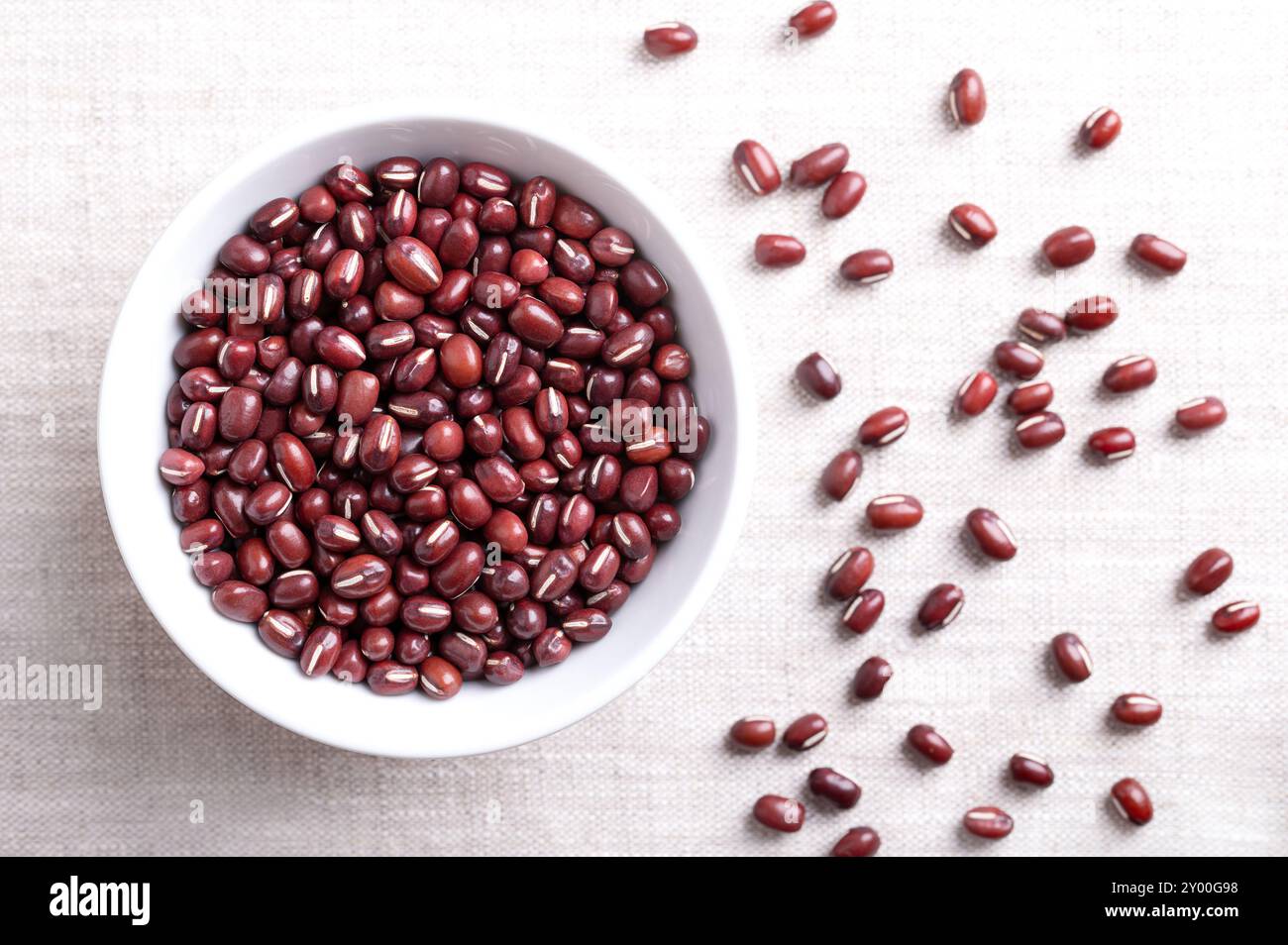 Haricots Adzuki dans un bol blanc sur tissu de lin. Aussi connu sous le nom azuki, aduki, rouge ou rouge haricot mung. Graines séchées de Vigna angularis. Banque D'Images