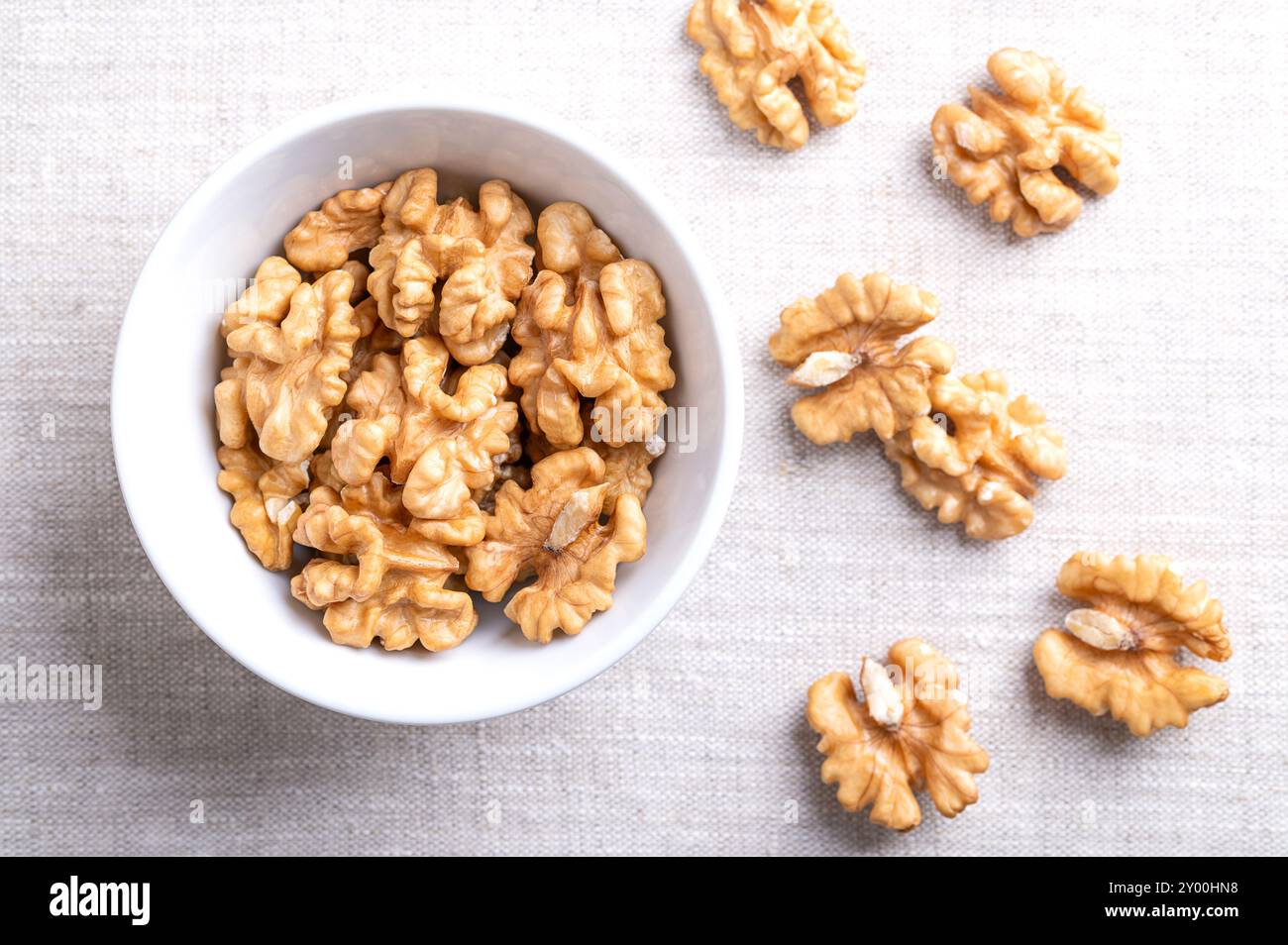 Demi-noyaux de noix dans un bol blanc sur tissu de lin. Moitiés décortiquées et séchées de cerneaux de noix, graines mûres de noyer commun Juglans regia. Banque D'Images