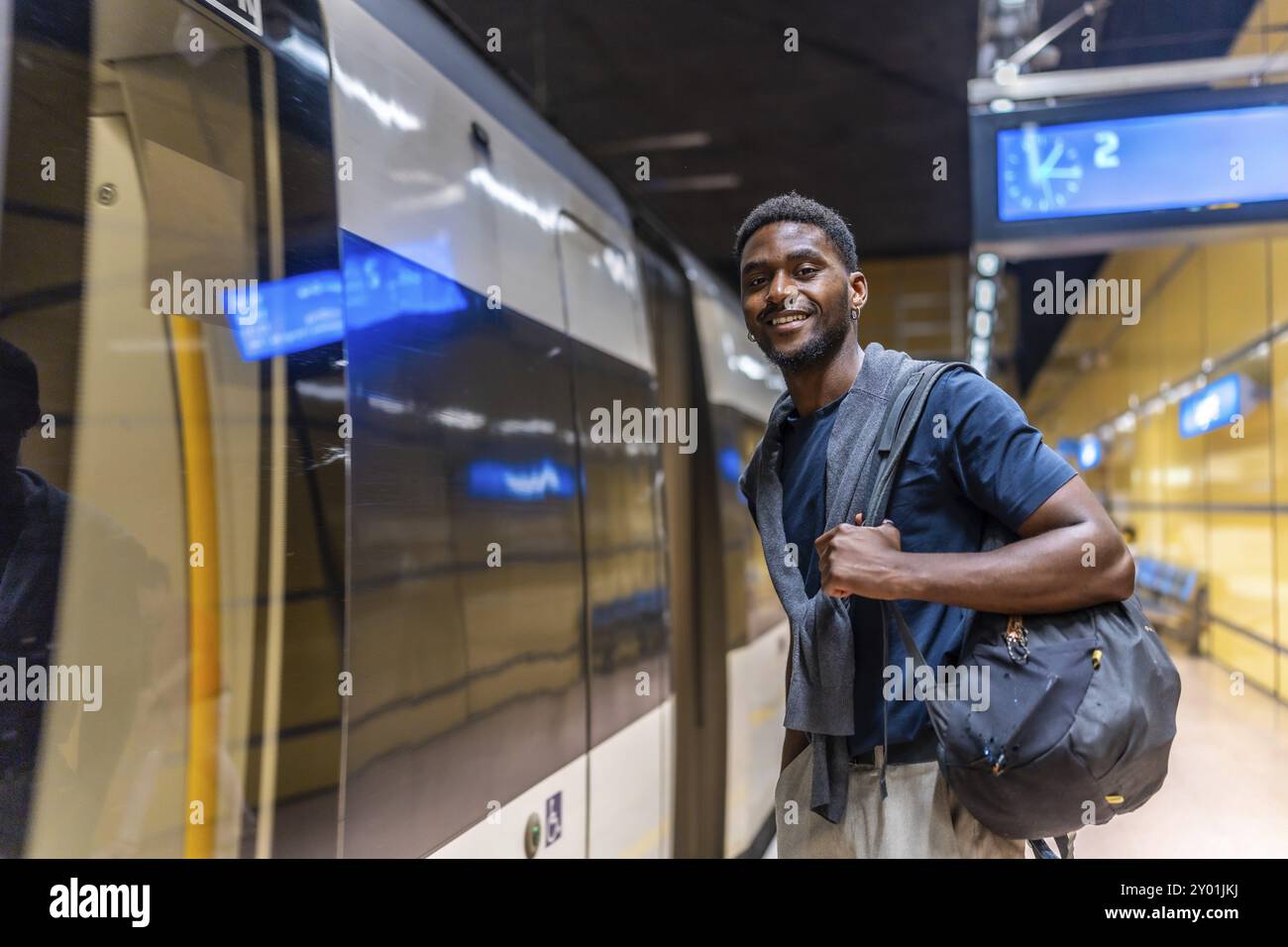 Jeune homme d'affaires africain attendant le métro la nuit debout sur le quai et souriant à la caméra Banque D'Images