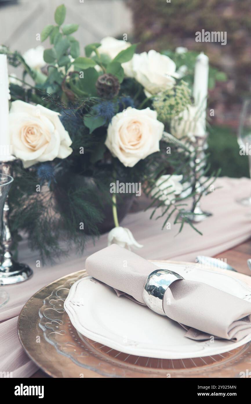 Bougies et vase avec des roses blanches placées sur la table ronde près des verres à vin pendant la date romantique dans le jardin Banque D'Images