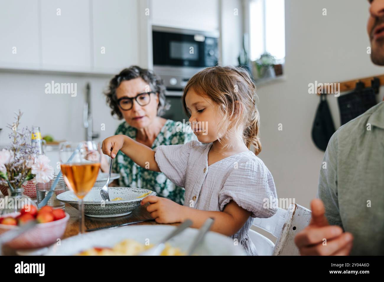 Fille mangeant le dîner tout en étant assis à la table à manger avec la famille à la maison Banque D'Images