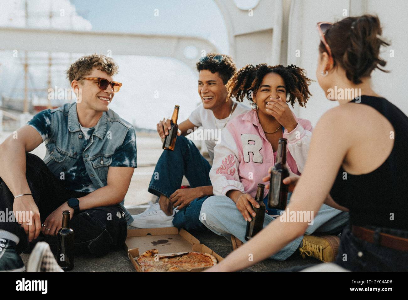 Heureux jeunes amis masculins et féminins ayant pizza avec de la bière tout en étant assis sur le sol au parking Banque D'Images