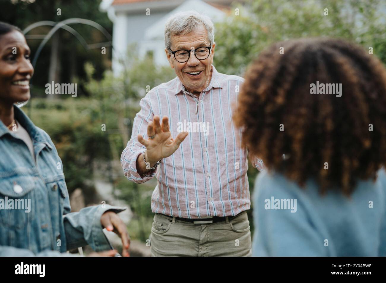 Homme senior souriant portant des lunettes et saluant des amis dans la fête de jardin Banque D'Images