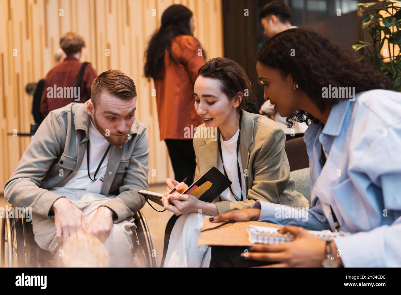 Jeune femme entrepreneure tenant un journal intime et discutant avec des professionnels des affaires au centre de congrès Banque D'Images