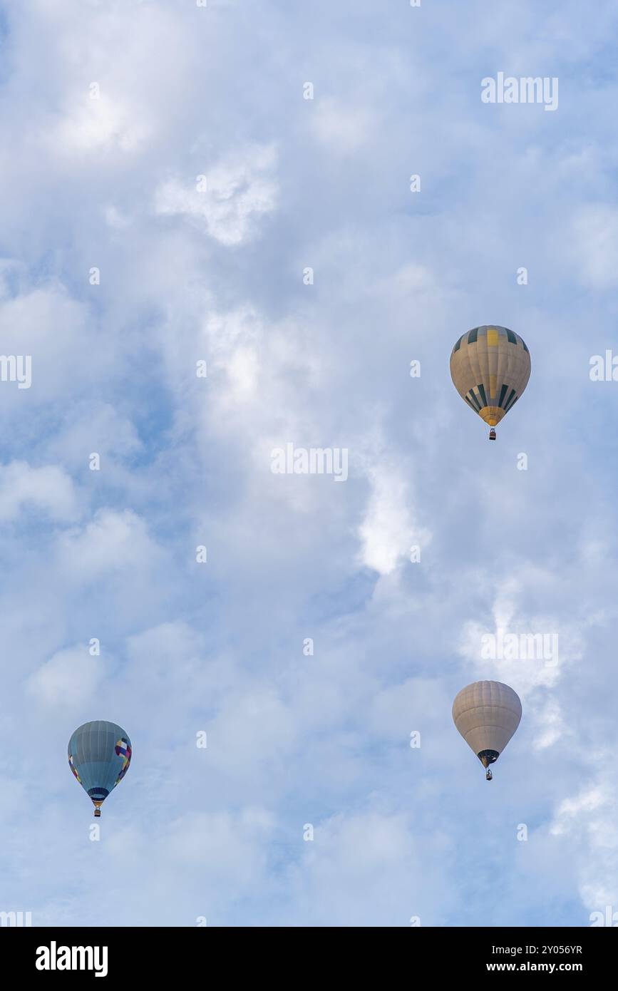 Trio de montgolfières vibrantes flotte à travers les nuages, participant à une compétition passionnante, mettant en vedette des designs colorés sur fond de cl Banque D'Images