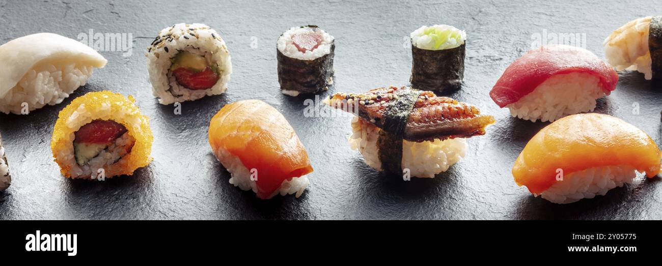Panorama sushi. Nigiri à l'anguille, saumon et thon, rouler à l'avocat et maki au concombre sur fond noir, cuisine japonaise sur une assiette chez un asiatique Banque D'Images