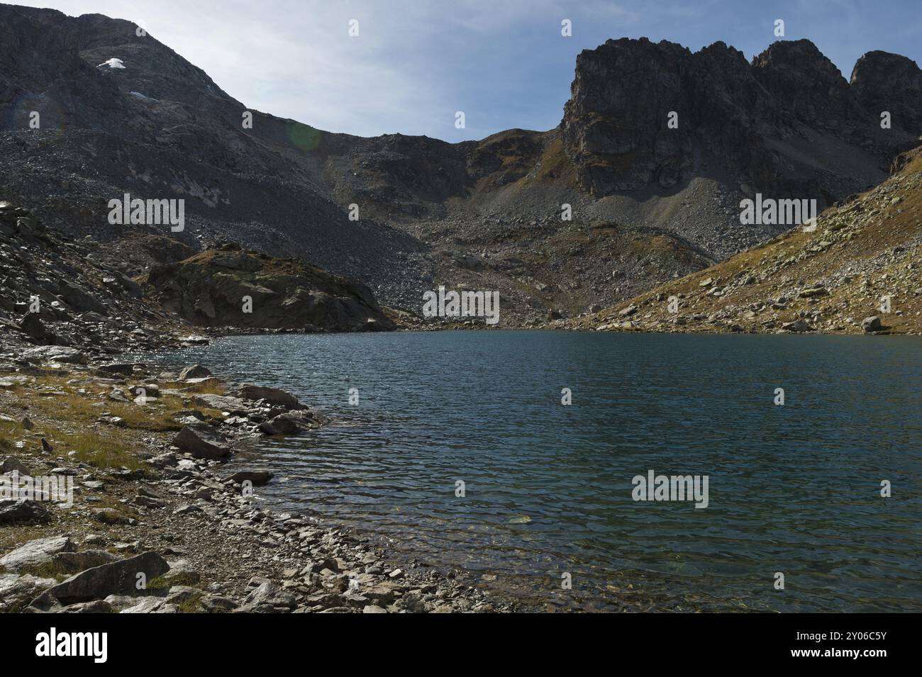 Paysage d'un lac de haute montagne avec la lumière du jour avec des pierres translucides à travers l'eau au fond du lac et des roches acérées en arrière-plan. Banque D'Images