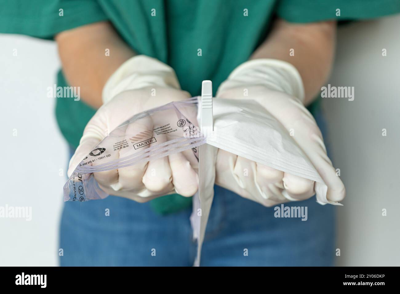 Femme médecin dans les vêtements de plaine ouvrant l'emballage médical. Gros plan des mains féminines avec des gants blancs ouvrant l'emballage. Banque D'Images