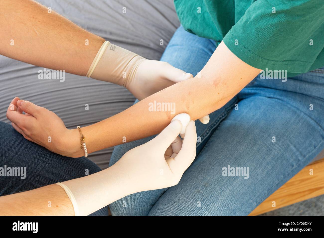 Docteur en vêtements de plaine traitant le bras d'une femme. Soins à domicile pour une fille. Médecin sans manteau blanc avec des gants blancs donnant des soins médicaux à domicile. Banque D'Images