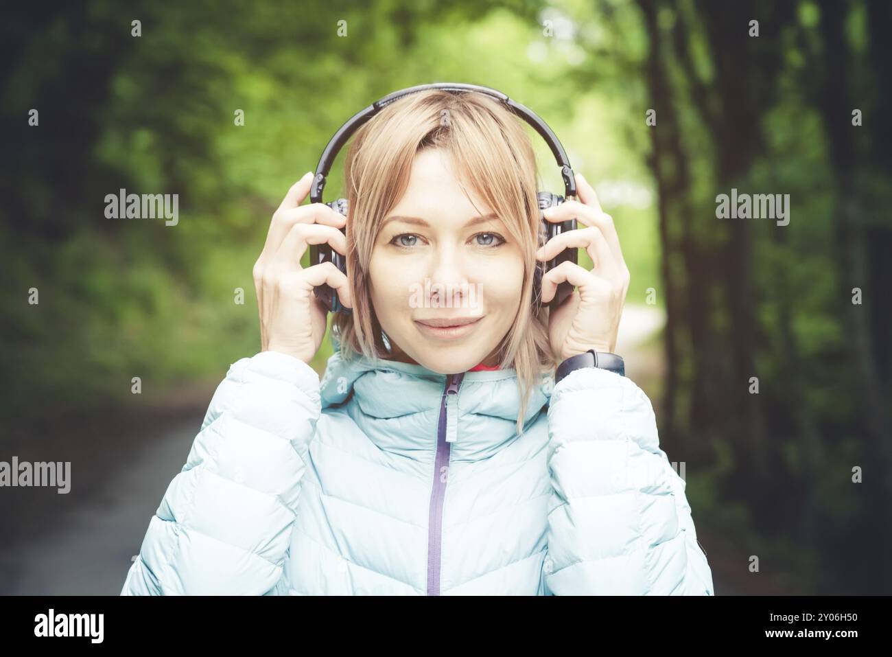 Portrait d'une fille de sport attrayante blonde dans une veste de descente légère habillant casque bluetooth avec de la musique ou les sons de la nature tout en étant sur Banque D'Images