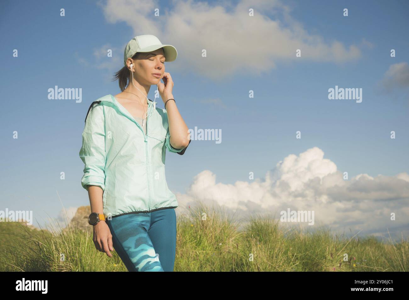 Femme coureuse de fitness écoutant de la musique sur la nature. Portrait de belle fille portant des écouteurs écouteurs et casquette de course. dans le contexte de Banque D'Images Femme coureuse de fitness écoutant de la musique sur la nature. Portrait de belle fille portant des écouteurs écouteurs et casquette de course. dans le contexte de Banque D'Images