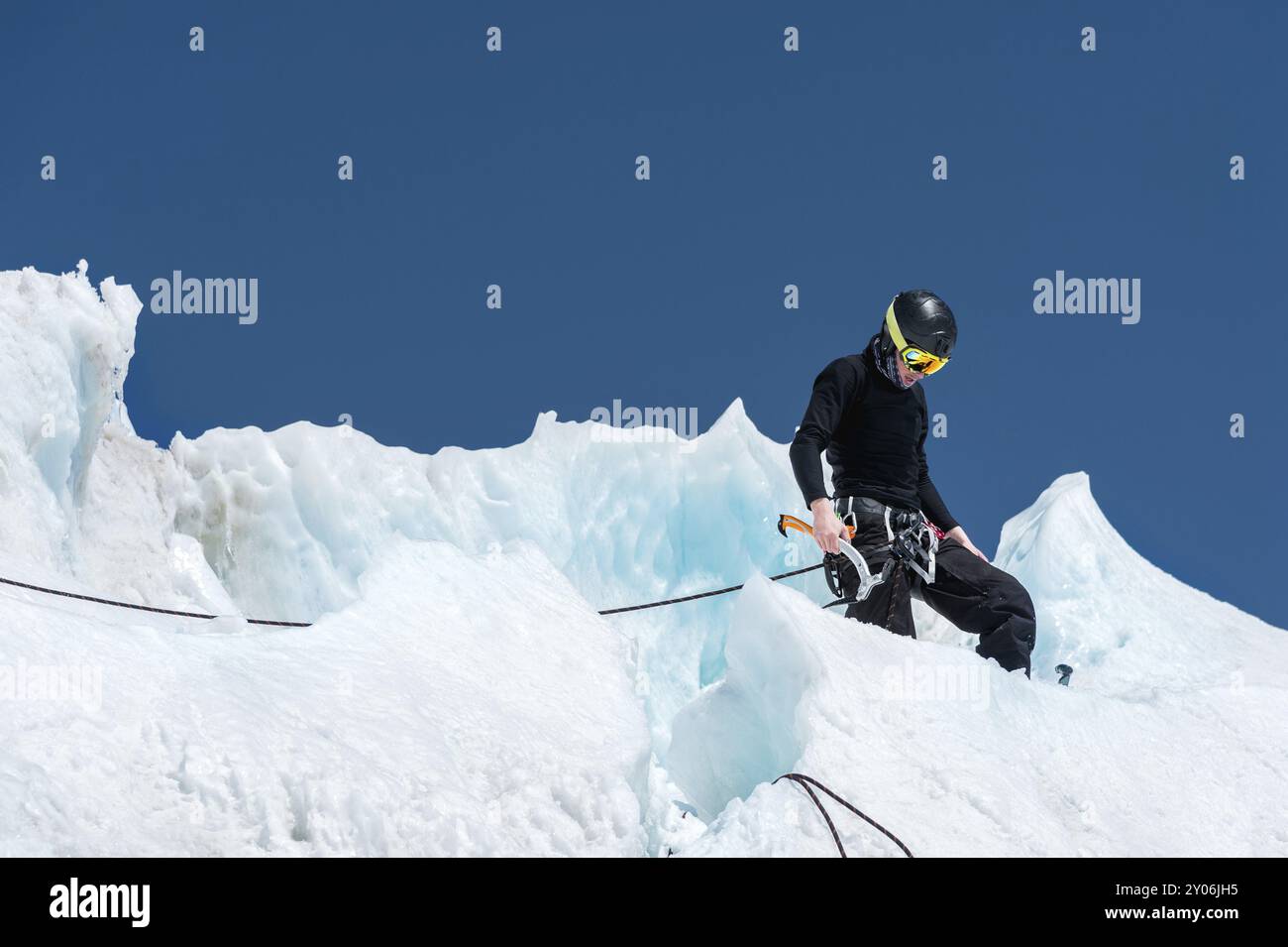 Un alpiniste professionnel portant un casque et un masque de ski sur l'assurance entaille la hache de glace dans le glacier. Le travail d'un grimpeur professionnel en Winte Banque D'Images