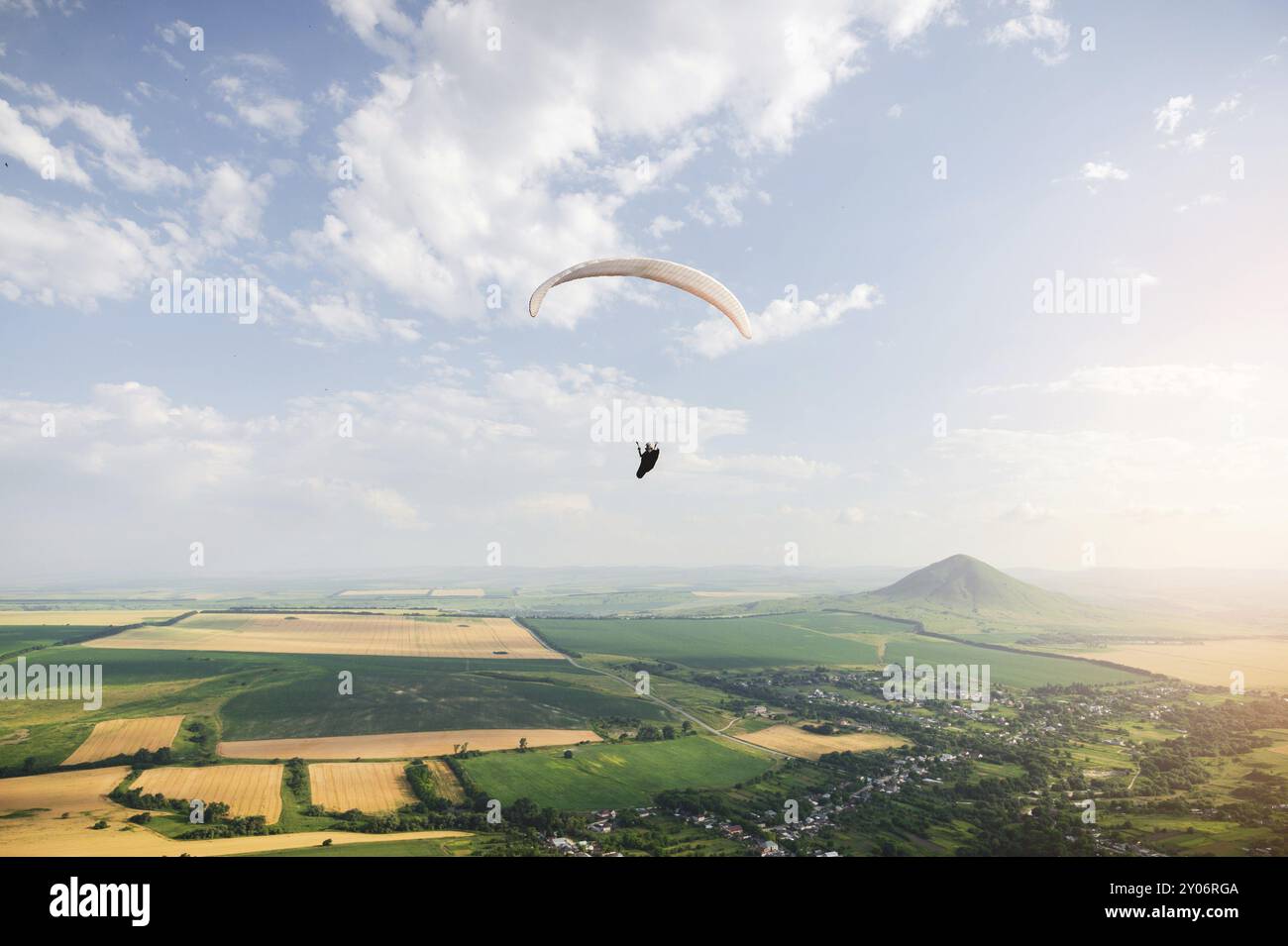Un parapente professionnel dans un cocon suit des mouches au-dessus du sol contre le ciel et les champs avec des montagnes Banque D'Images Un parapente professionnel dans un cocon suit des mouches au-dessus du sol contre le ciel et les champs avec des montagnes Banque D'Images