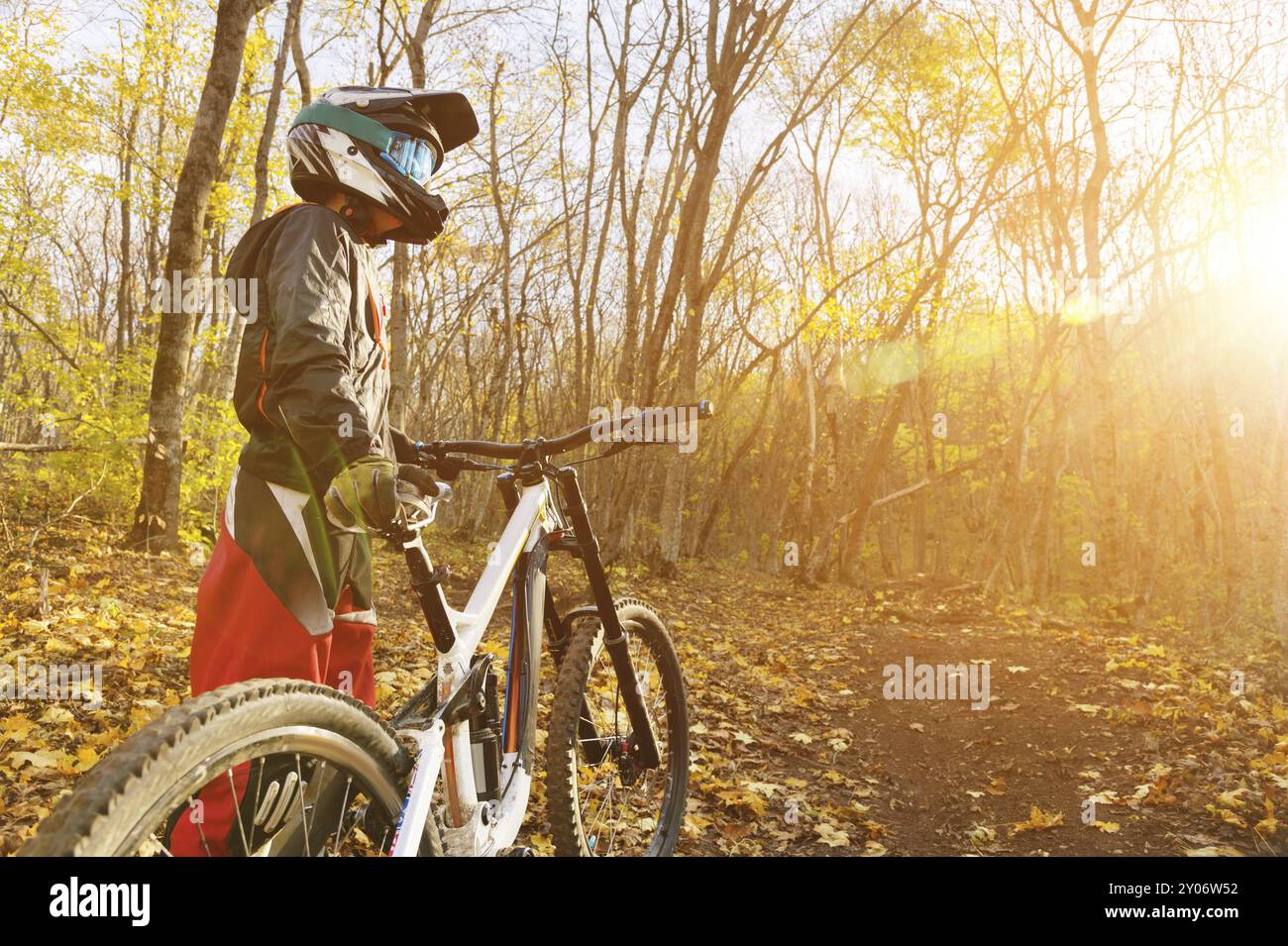 Portrait d'un jeune cavalier en pleine protection d'un masque de casque intégral et de gants sur un vélo dans une forêt d'automne avec des feuilles jaunes. Le concept de Banque D'Images