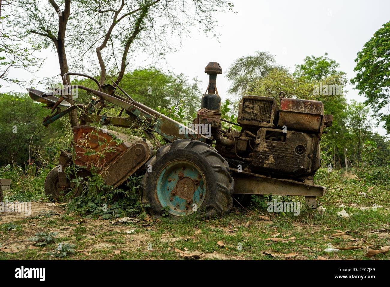 Un vieux motoculteur rouillé envahi par la végétation, abandonné dans une zone boisée avec des arbres et des arbustes en arrière-plan Banque D'Images