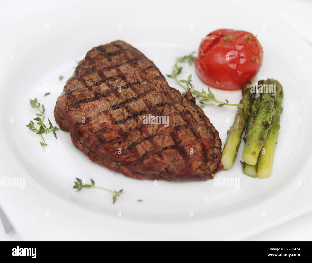 Steak de bœuf avec asperges cuites et tomate sur assiette blanche Banque D'Images