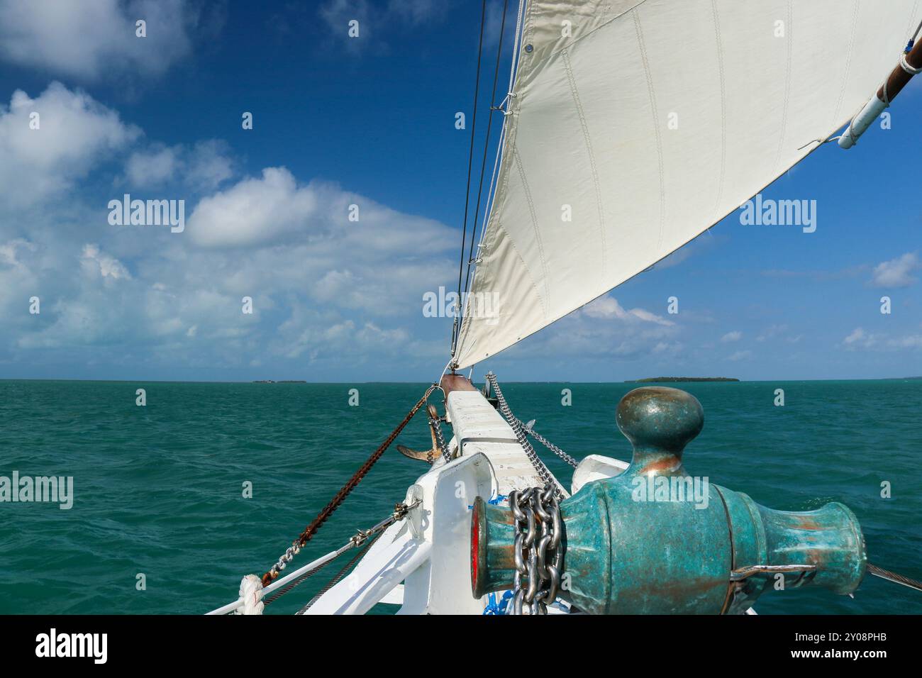 La voile vibrante est capturée à mi-bouffée, laissant entendre un vent vif poussant le navire vers l'avant, une vue rapprochée de la voile d'un voilier par une journée ensoleillée. Banque D'Images