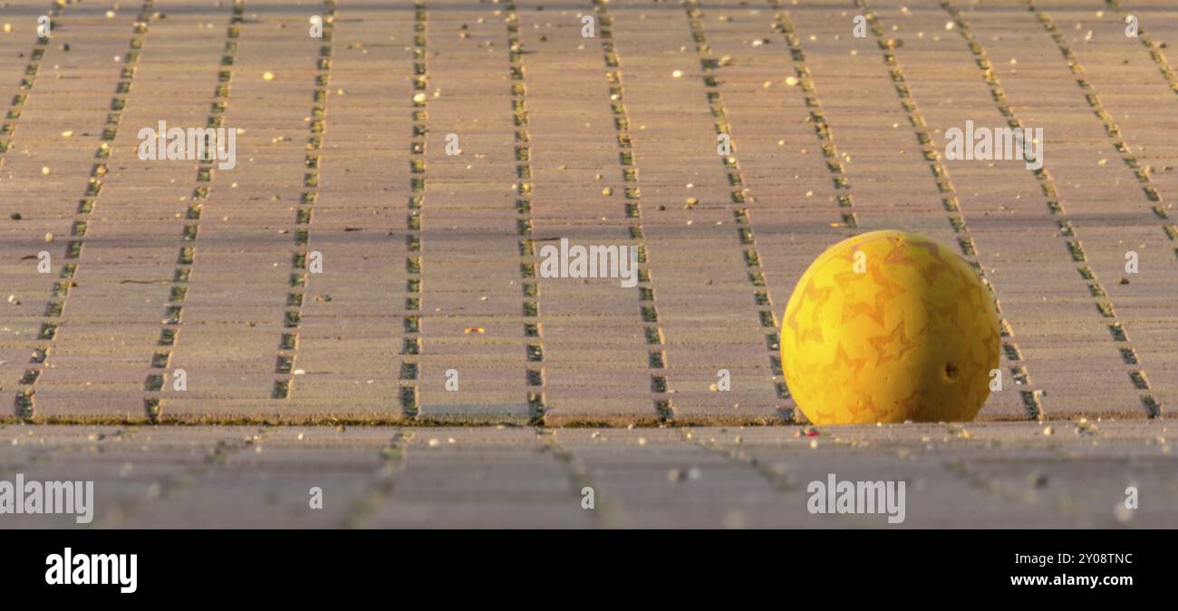 Balle jaune pour enfants couchée sur un carré pavé sur un fond flou Banque D'Images