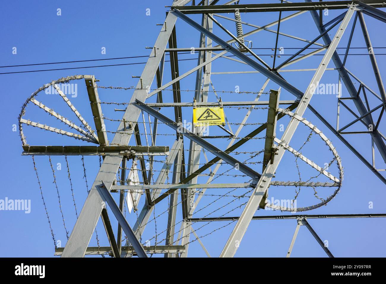 Gros plan d'une tour de transmission électrique métallique avec un panneau d'avertissement haute tension contre un ciel bleu clair sans nuages. Banque D'Images