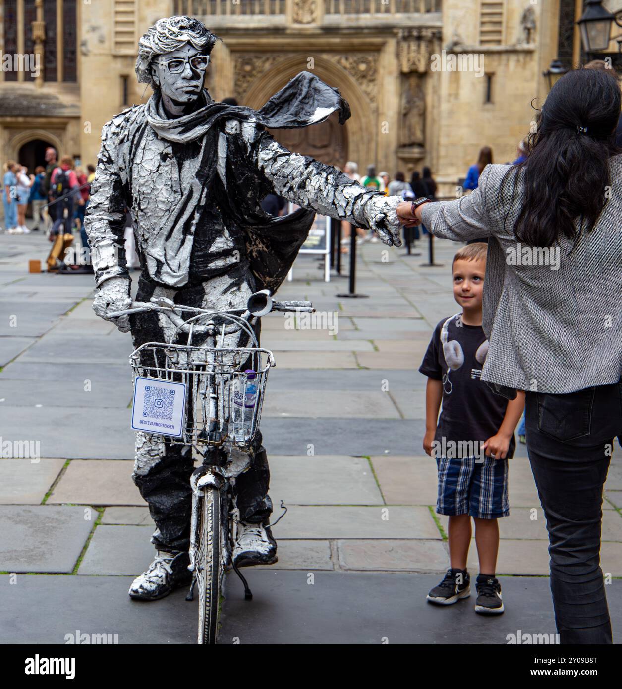 Un artiste vêtu d'un costume unique et accrocheur monte sur un vélo blanc devant le bâtiment historique de la salle des pompes, en observant les passants. Banque D'Images