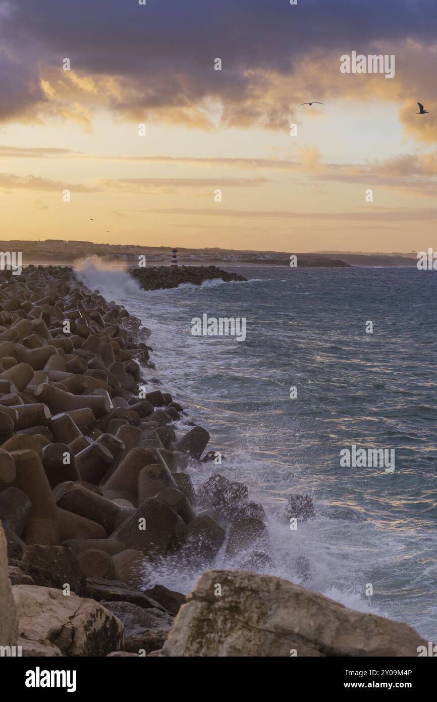 Phare de Peniche avec plage de Supertubos en arrière-plan au coucher du soleil avec des vagues qui s'écrasant, au Portugal Banque D'Images