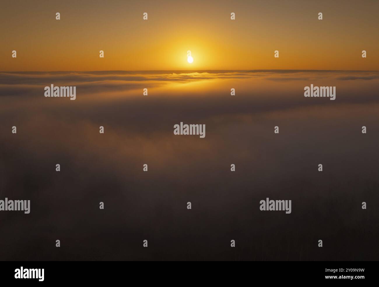 Le soleil se couche sur un horizon de nuages, projetant des teintes orange et or à travers le ciel et l'atmosphère brumeuse, Nord, Alberta, Canada, Amérique du Nord Banque D'Images