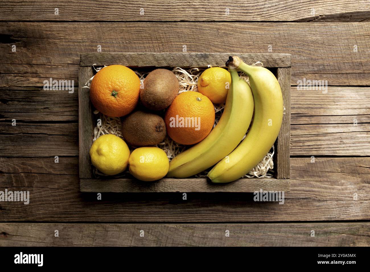 Fruits tropicaux frais dans une boîte de livraison en bois sur fond de bois. Orange, banane, kiwi et citron vue sur le dessus plat avec espace pour copier un peu plus Banque D'Images