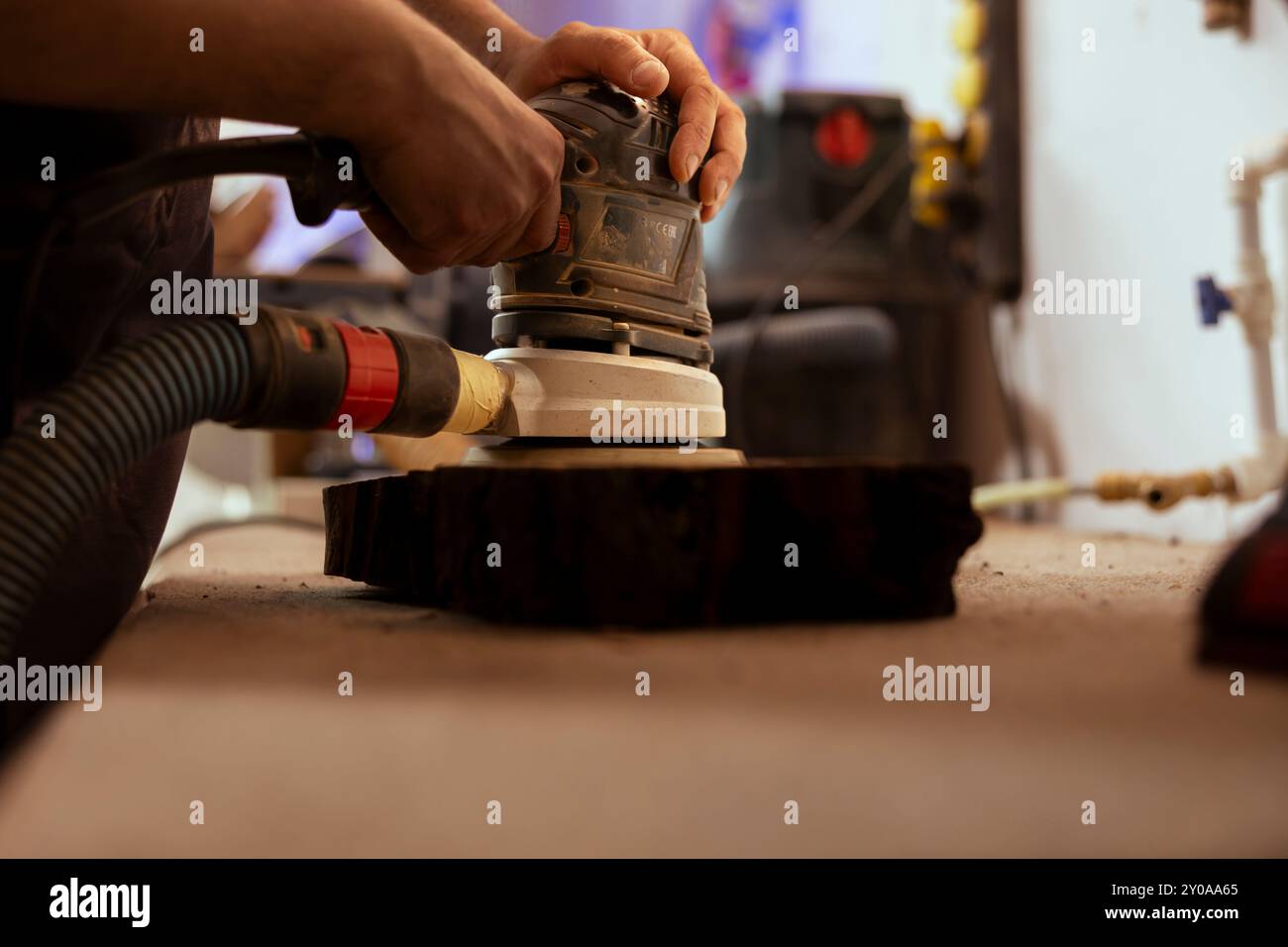 Menuisier utilisant une ponceuse orbitale avec du papier abrasif fin sur la pièce de bois pour obtenir une finition raffinée. Fabricant utilisant la meuleuse d'angle sur le bloc de bois pour des résultats professionnels, gros plan Banque D'Images