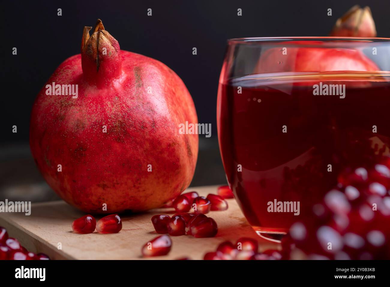 Jus de grenade aigre-douce dans un verre transparent sur la table, à côté de lui se trouvent des grenades mûres rouges avec de gros grains sucrés Banque D'Images