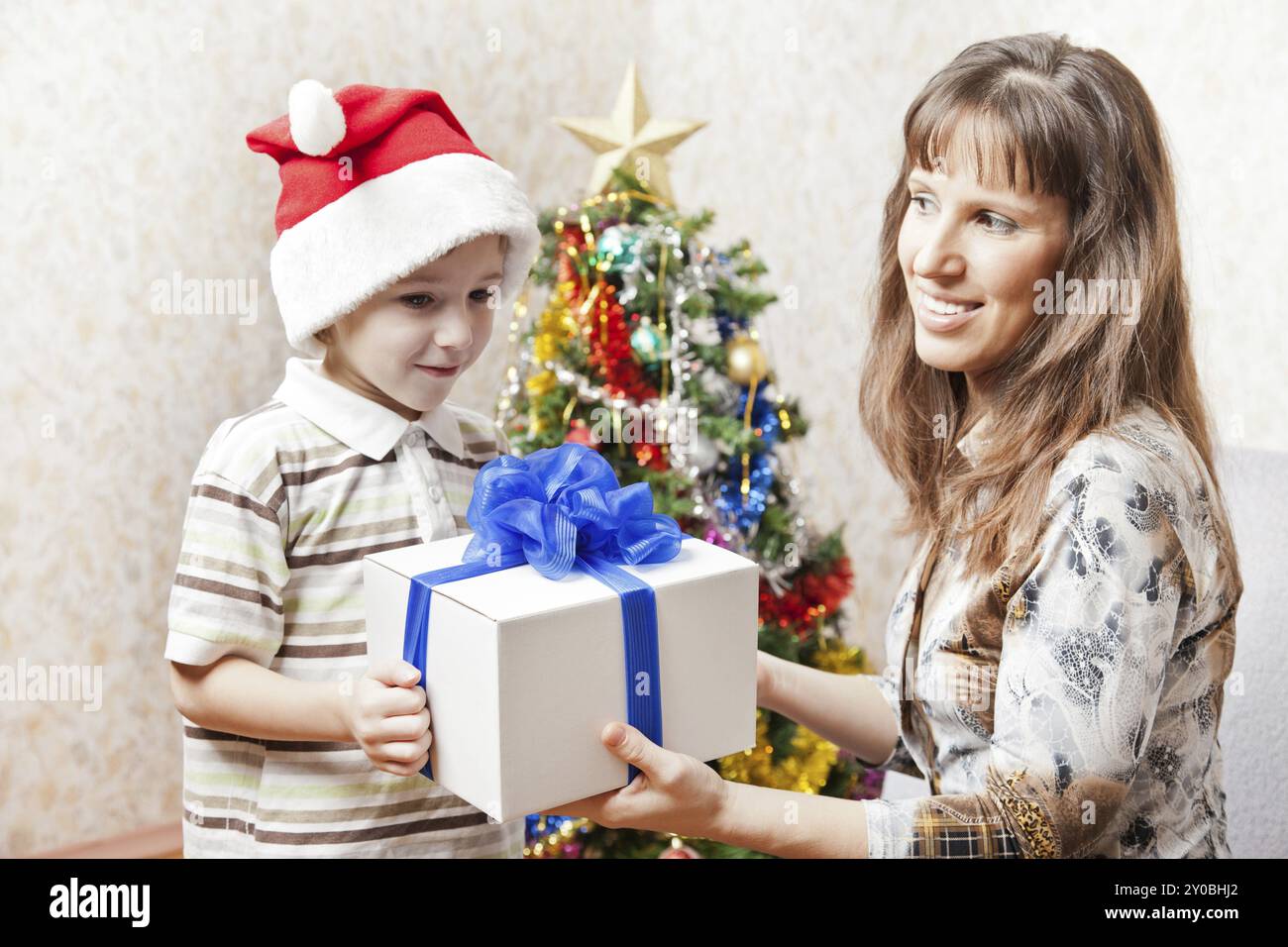 Mère souriante donnant un cadeau de nouvel an ou une boîte cadeau de vacances de noël au petit fils portant le chapeau du Père Noël Banque D'Images