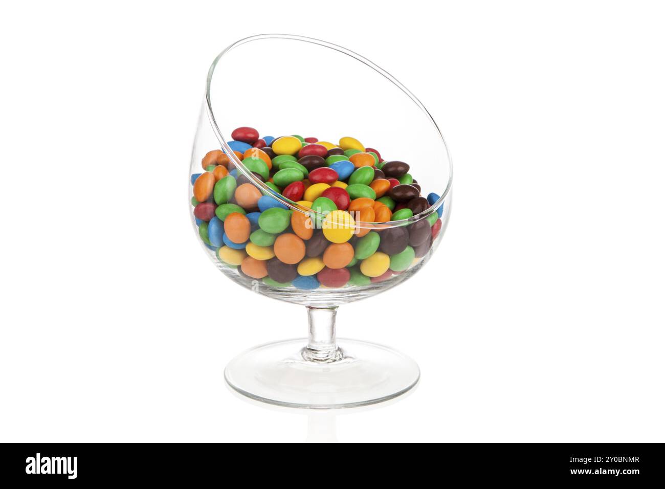 Bonbons doux colorés gouttes dragées dans le verre incliné isolé sur blanc avec réflexion Banque D'Images