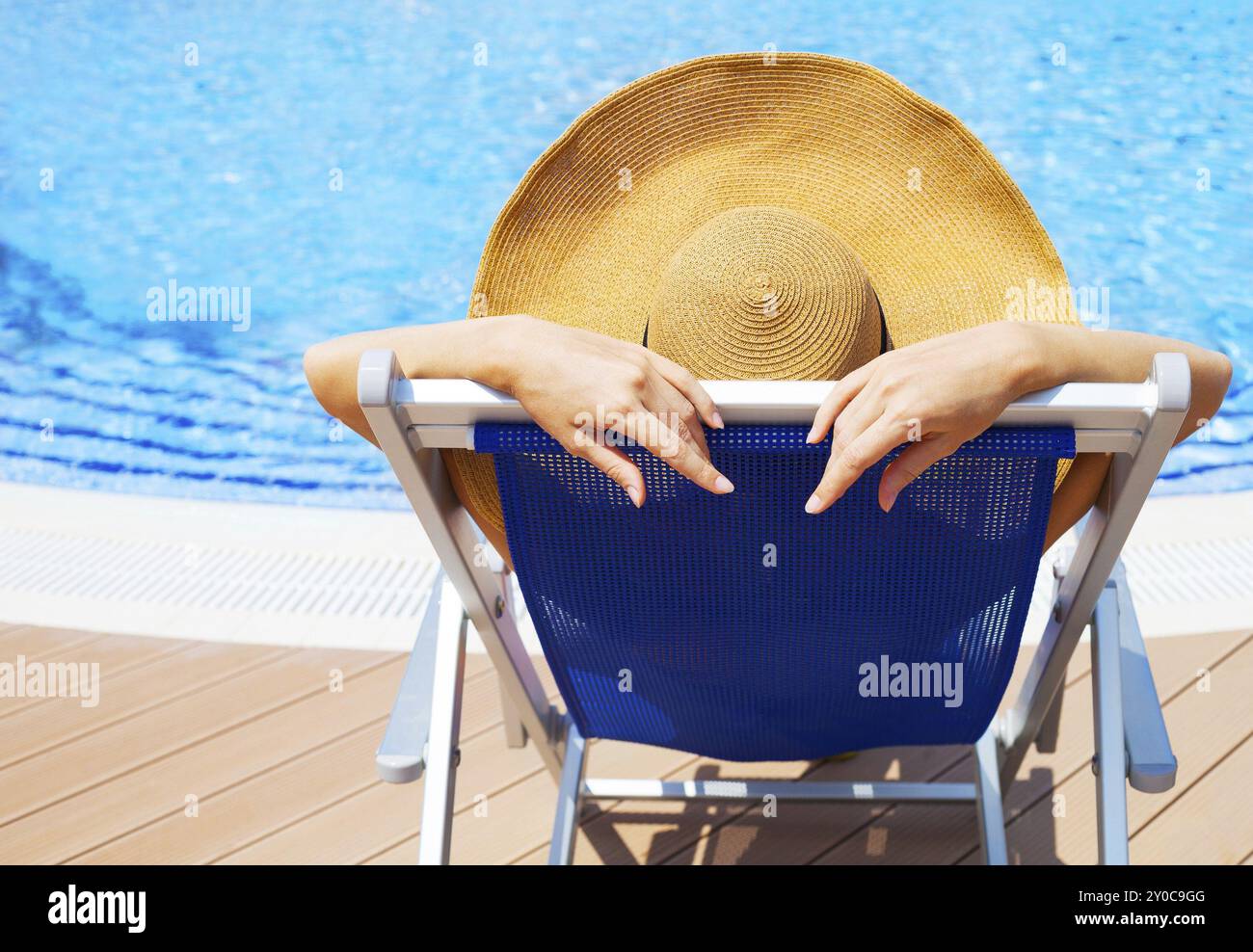 Belle jeune femme portant hat allongé sur un transat par piscine Banque D'Images