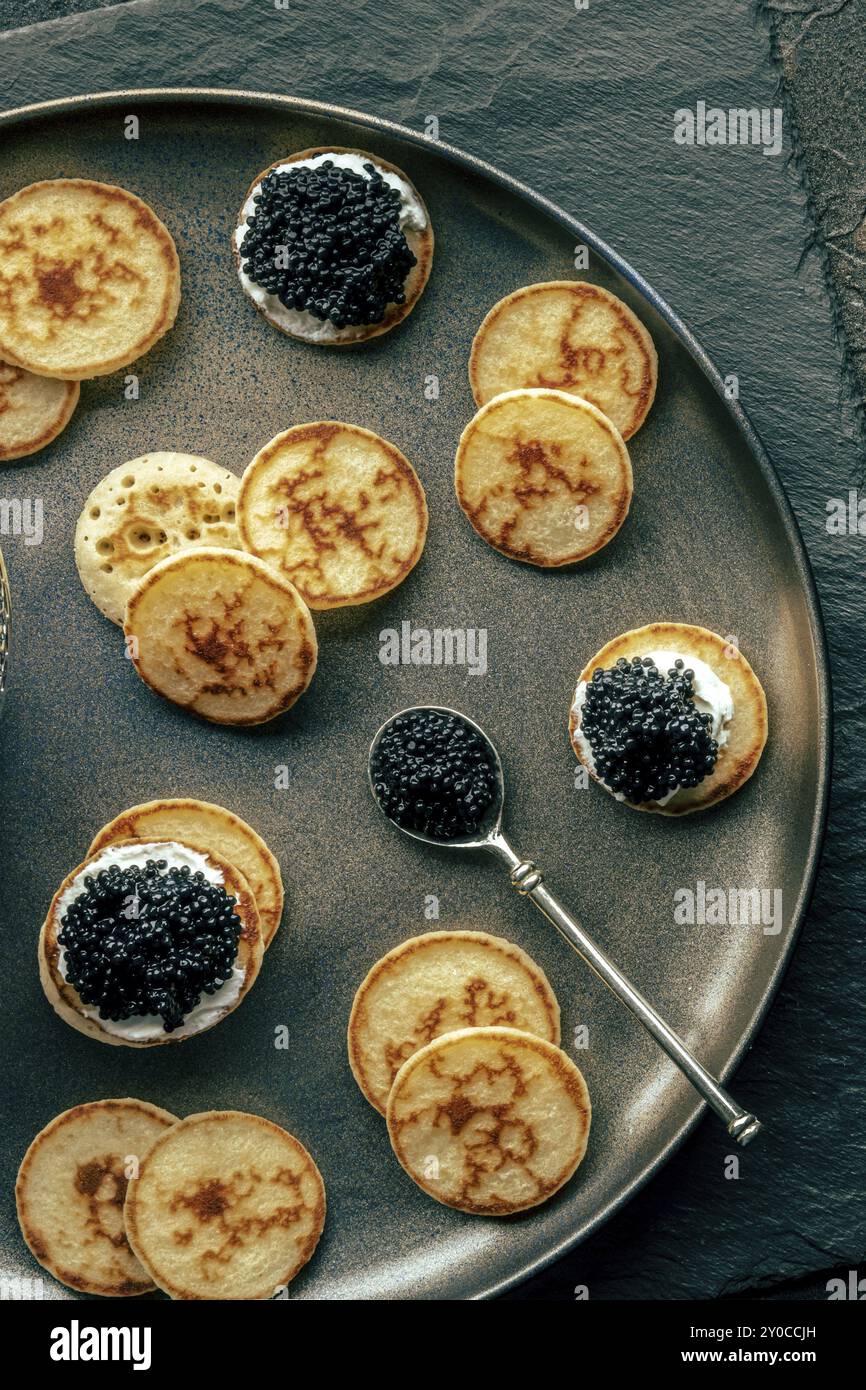 Blinis au caviar noir et au fromage à la crème, photographiés d'en haut, mini crêpes, un apéritif élégant, photographie culinaire Banque D'Images