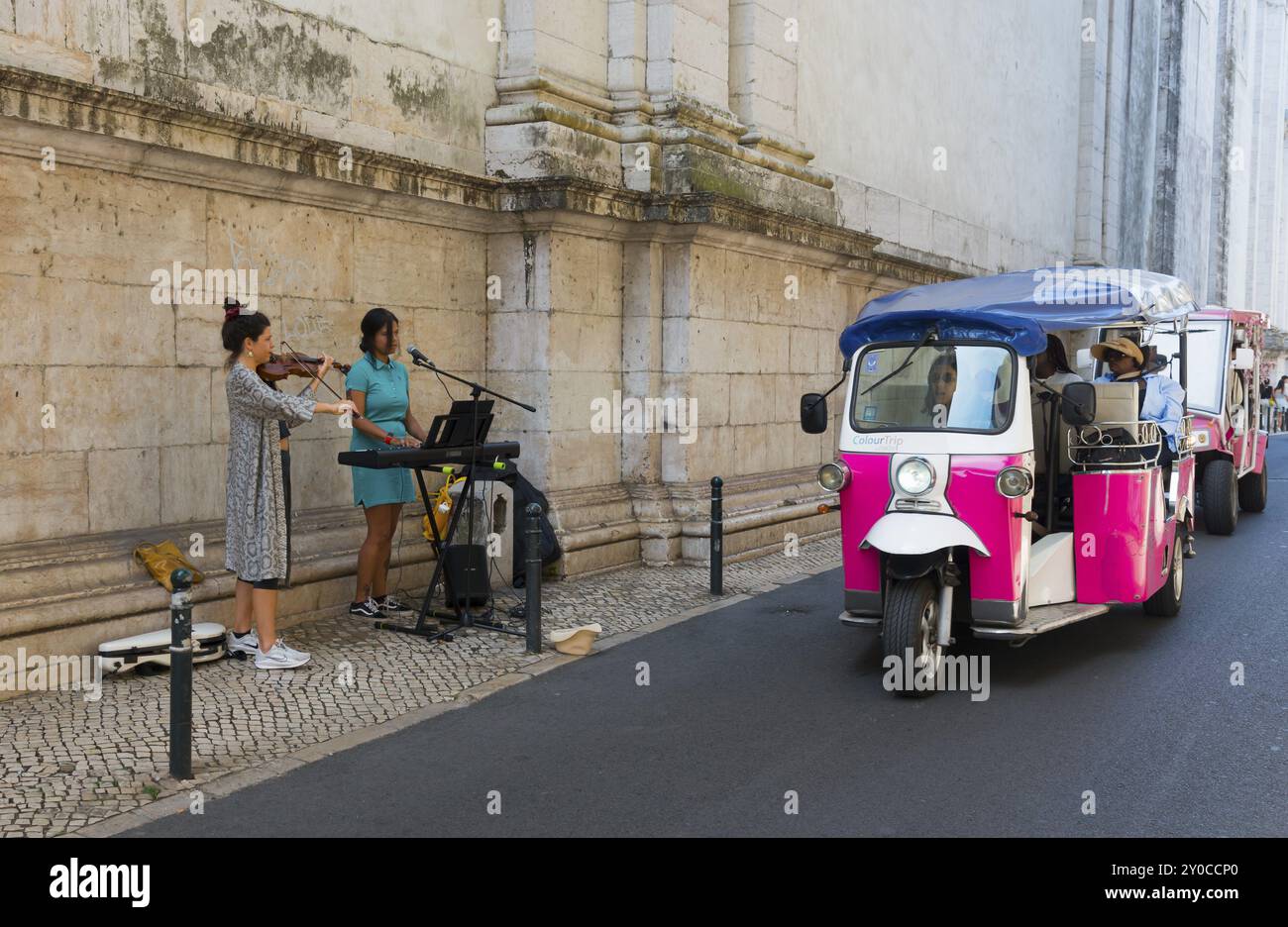 Un violoniste et un chanteur jouent de la musique devant un vieux mur tandis qu'un tuk-tuk rose passe, vieille ville, Lisbonne, Lisboa, Portugal, Europe Banque D'Images