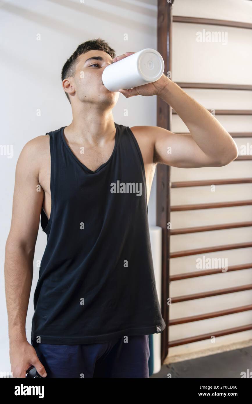 Un gymnaste dans un gymnase boit de l'eau d'une bouteille en métal pour s'hydrater Banque D'Images