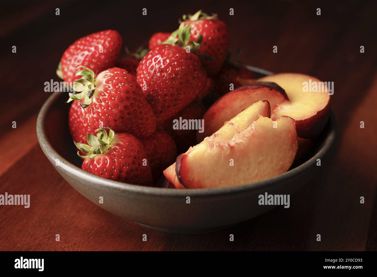 Une photo studio d'un bol de fraises fraîches et de pêches tranchées Banque D'Images