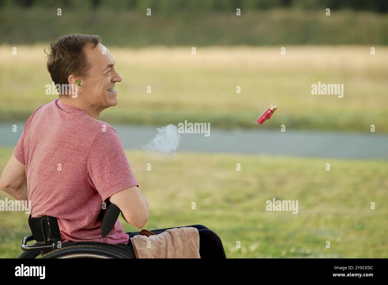 Un homme âgé dans un fauteuil roulant ouvre son fusil de chasse pour recharger les munitions, avec des douilles d'obus volant hors du canon dans le cadre Banque D'Images