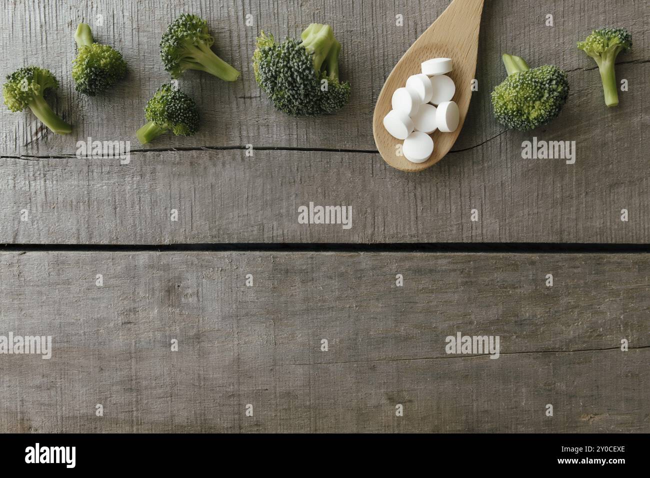 Capsules de vitamines ou de médicaments, brocoli sur cuillère en bois sur fond en bois. Thérapie de santé ou concept de traitement. Pilules vitaminiques. Banque D'Images