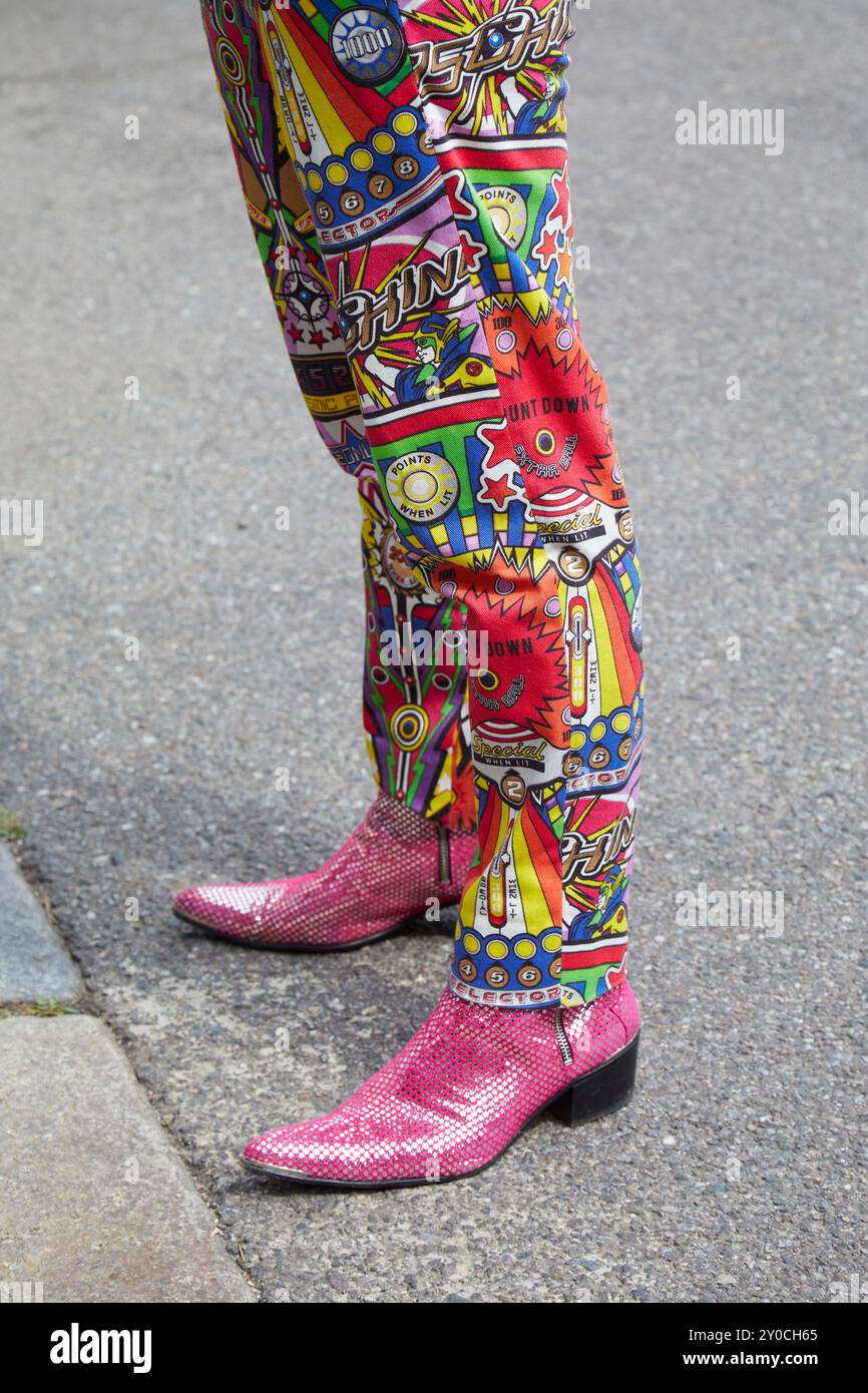 MILAN, ITALIE - 14 JUIN 2024 : homme avec un pantalon Moschino coloré et des bottes à paillettes roses avant le défilé Moschino, dans le style de rue Milan Fashion week Banque D'Images