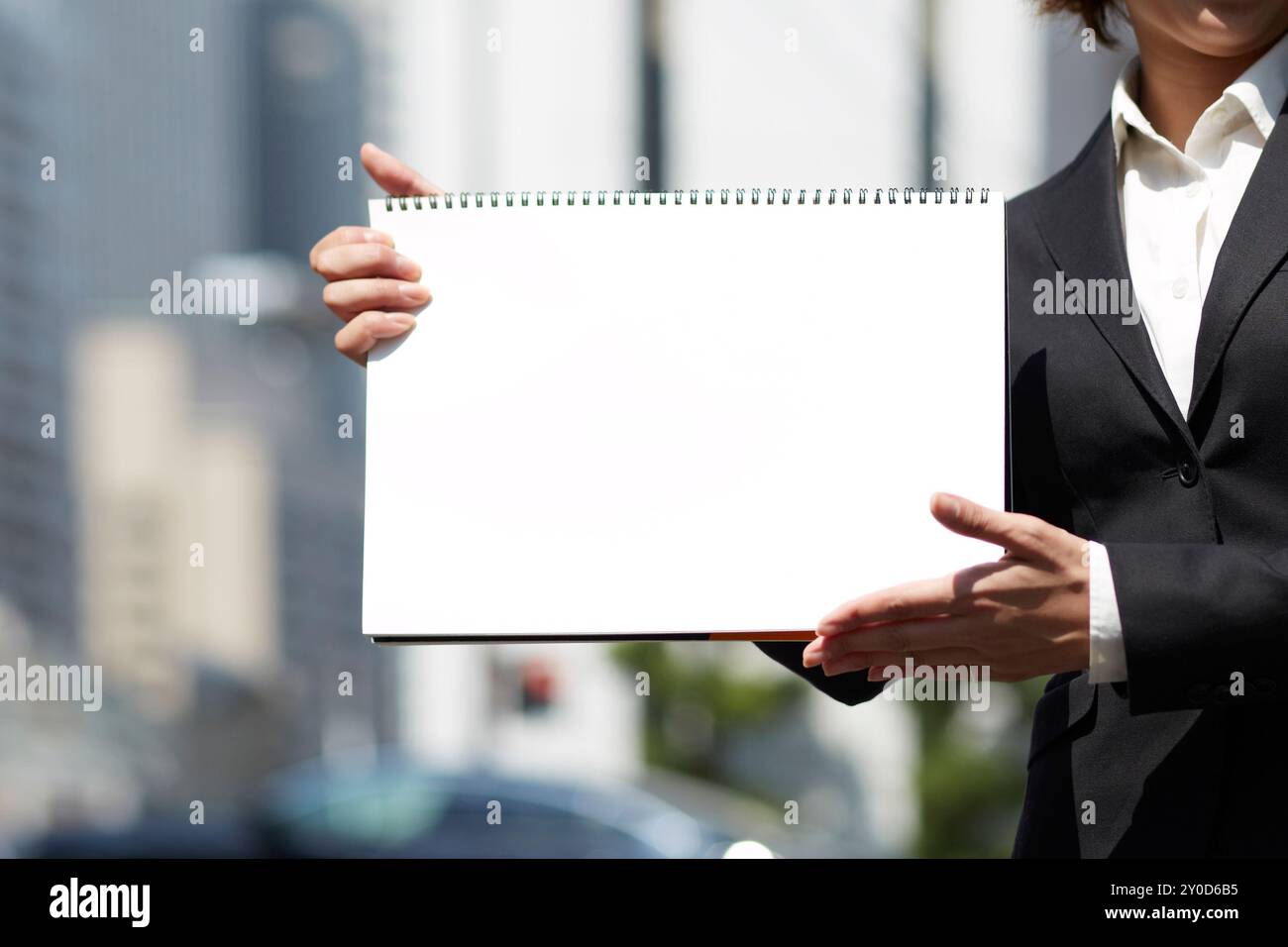 Une femme vêtue de costumes et tenant un carnet de croquis blanc soutenu par des bâtiments Banque D'Images