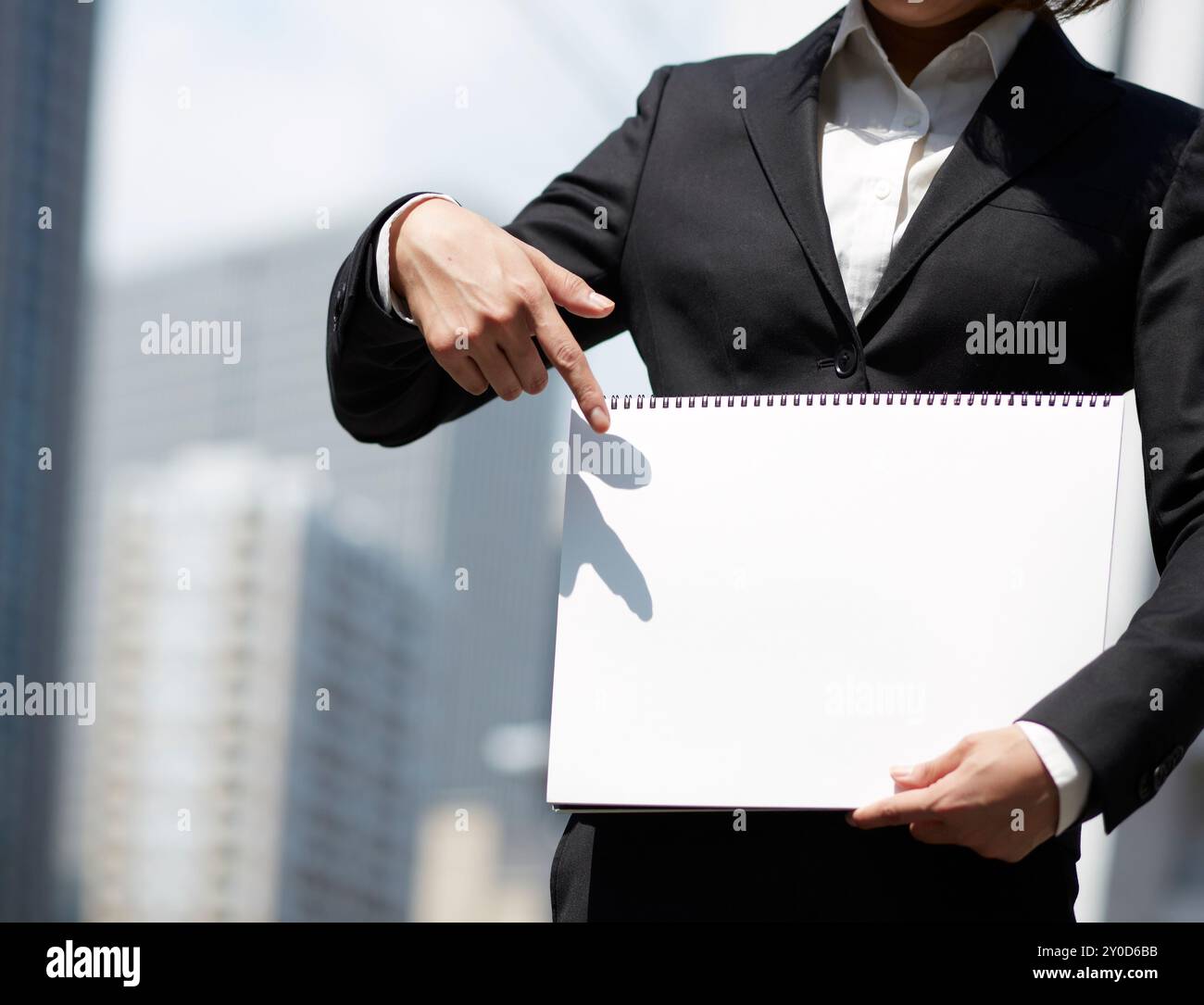 Une femme vêtue de costumes et pointant un carnet de croquis blanc soutenu par des bâtiments Banque D'Images