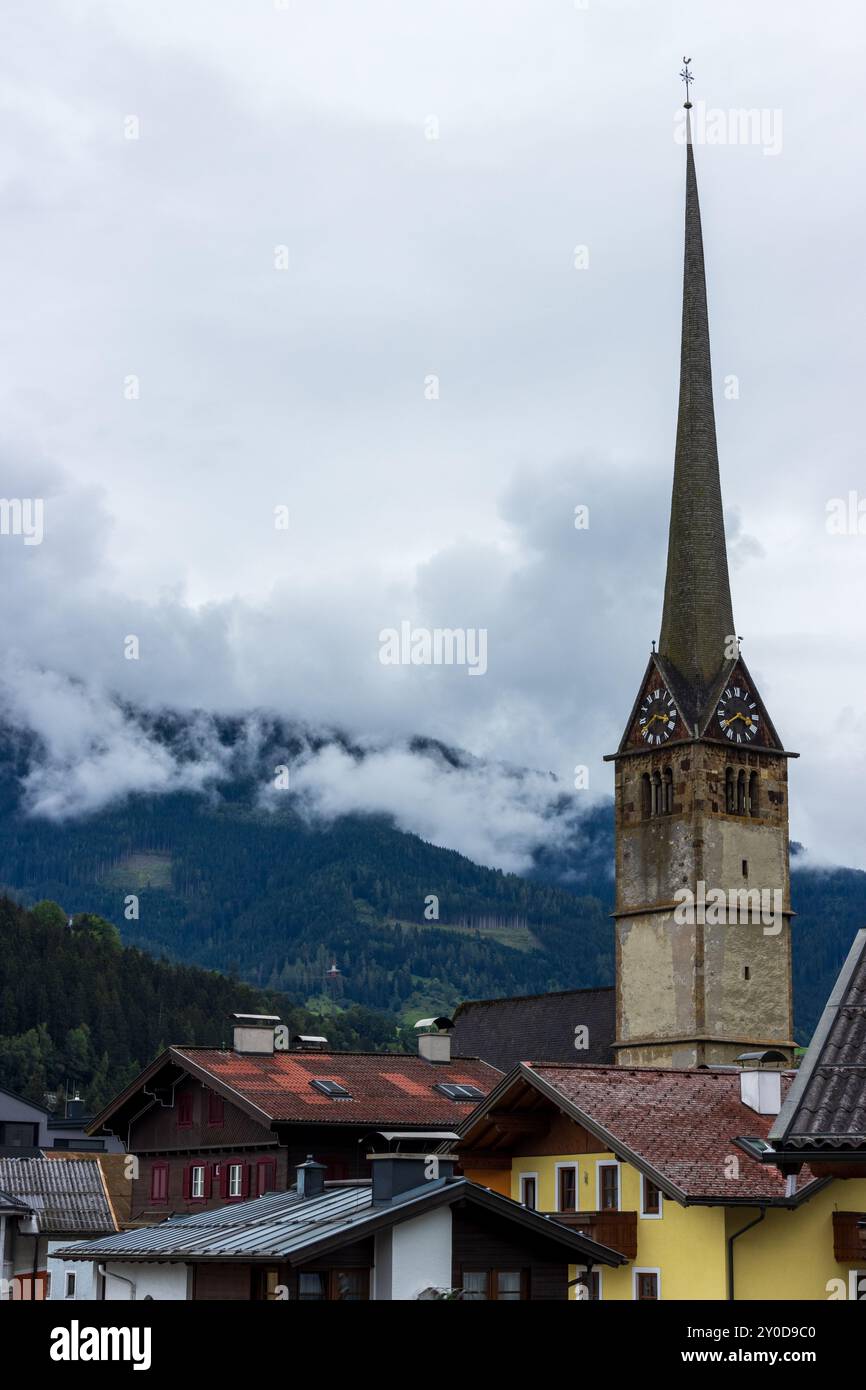 La belle flèche d'une église à Bischofshofen, Autriche dans les superbes Alpes autrichiennes, avec des nuages bas suspendus sur les forêts de montagne derrière. Banque D'Images