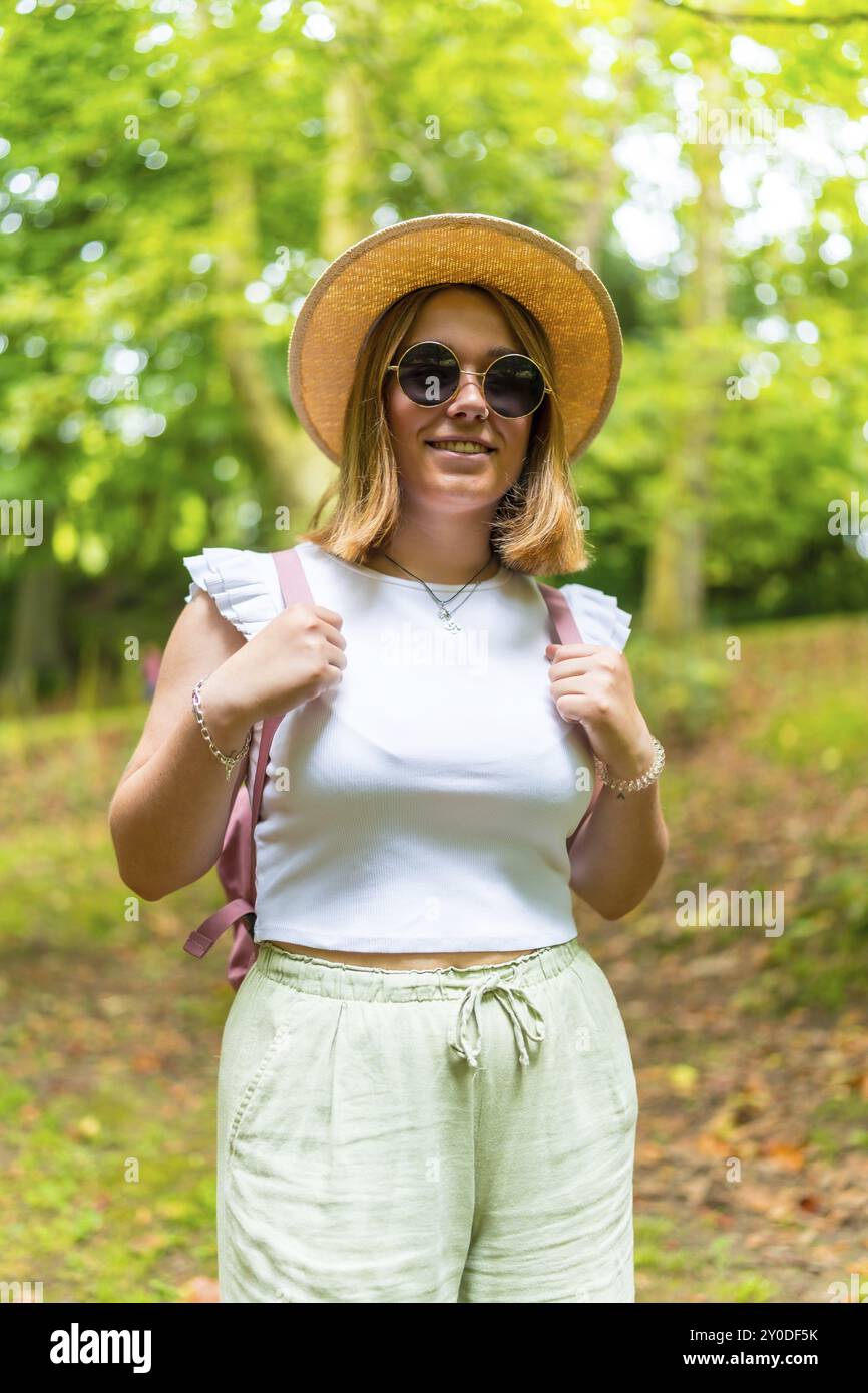 Portrait vertical d'une jeune femme adulte caucasienne en vêtements d'été et lunettes de soleil souriant lors d'une randonnée dans la forêt Banque D'Images