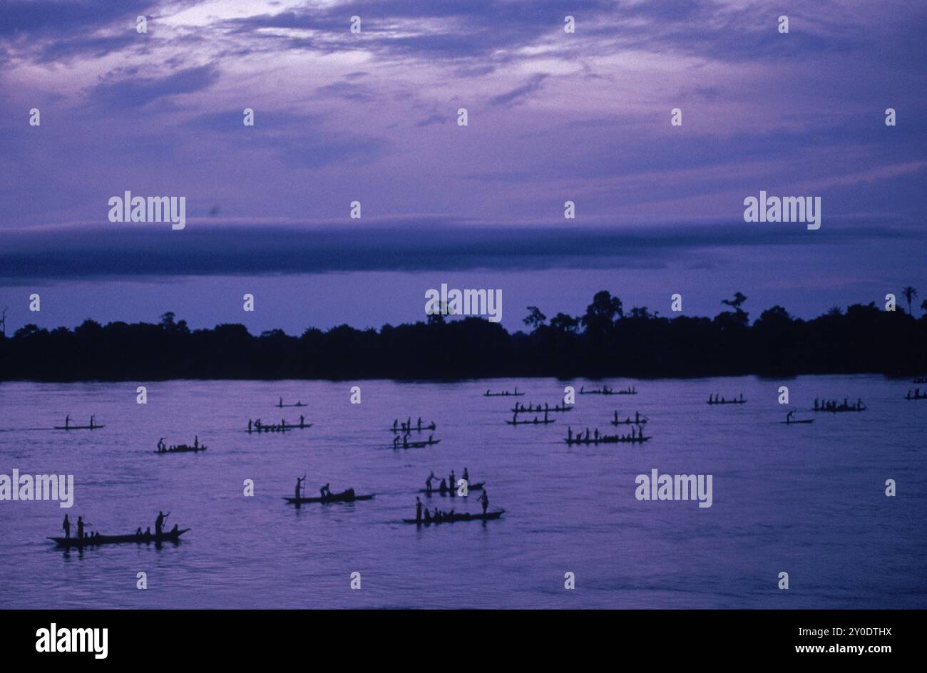 Les gens dans de grands canoës ou pirogues pagayent chez eux sur le fleuve Congo au crépuscule. Banque D'Images