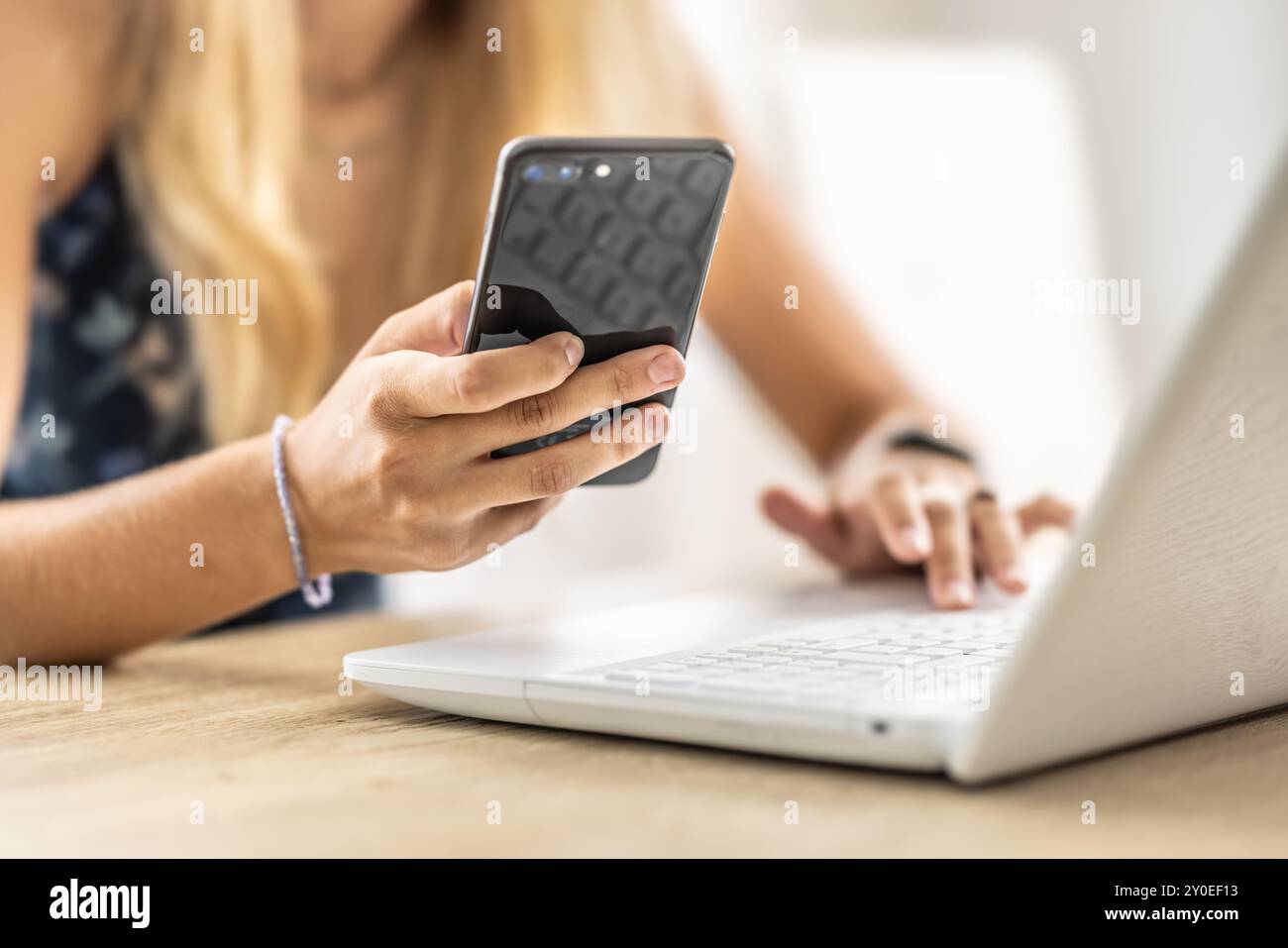 Une femme responsable tient un smartphone dans sa main et prend des notes sur l'ordinateur portable. Banque D'Images