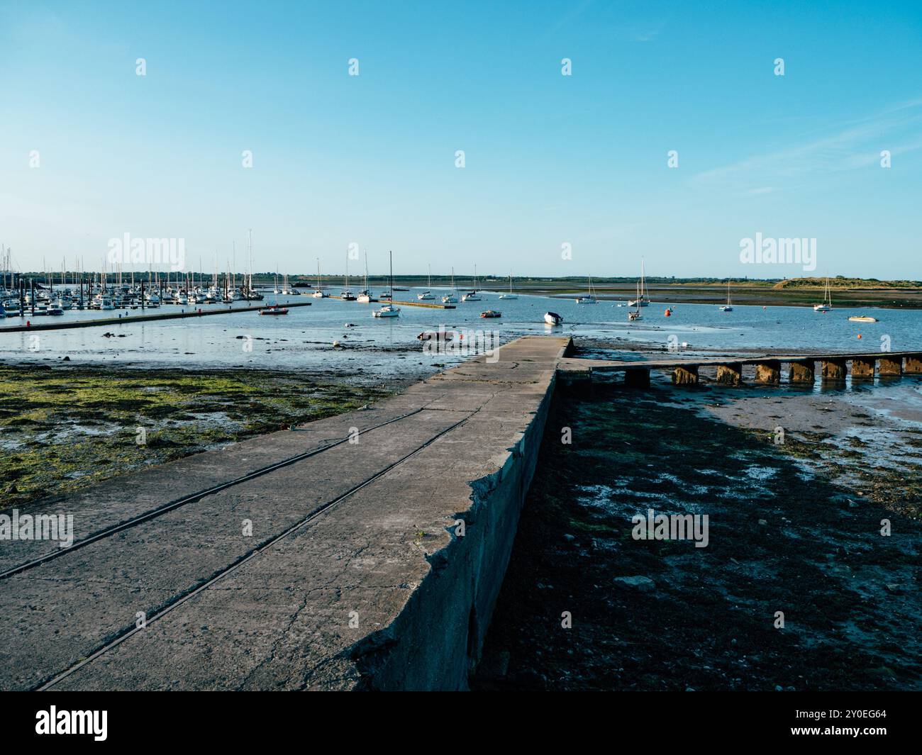 Le front de mer offre une large vue sur les bateaux amarrés à marée basse, avec la surface calme reflétant le ciel bleu et les collines lointaines sous la lumière du soleil Banque D'Images