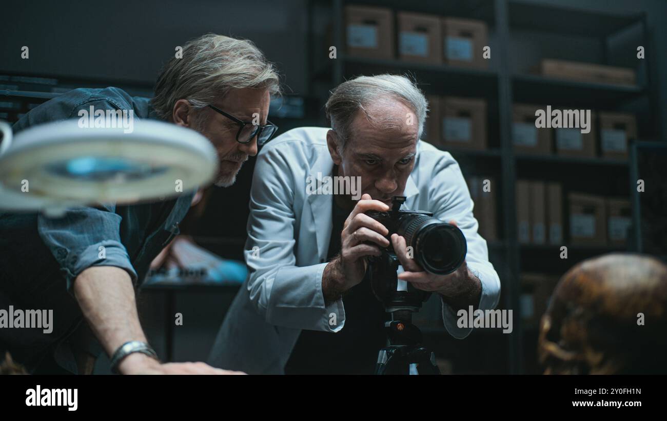 Laboratoire archéologique moderne : deux archéologues ont installé un appareil photo professionnel pour photographier des restes fossiles, avoir des discussions. Le scientifique senior en blouse de laboratoire prend des photos avec flash. Concept archéologique. Banque D'Images