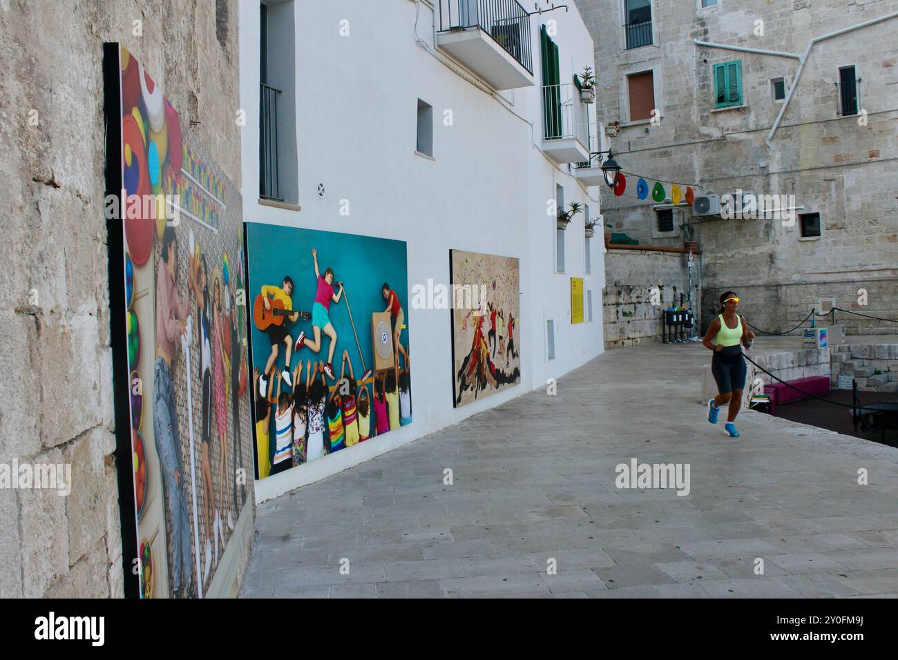 Jan von Hollebens photographie tirages accrochés sur le mur de la ville à monopoli italie pendant PhEST 2024 comme les joggeurs courent devant Banque D'Images