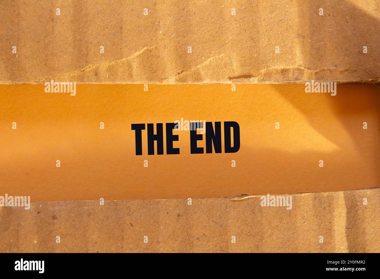 Le message de fin écrit sur du papier cartonné déchiré déchiré avec un fond orange. Conceptuel le symbole de fin. Copier l'espace. Banque D'Images
