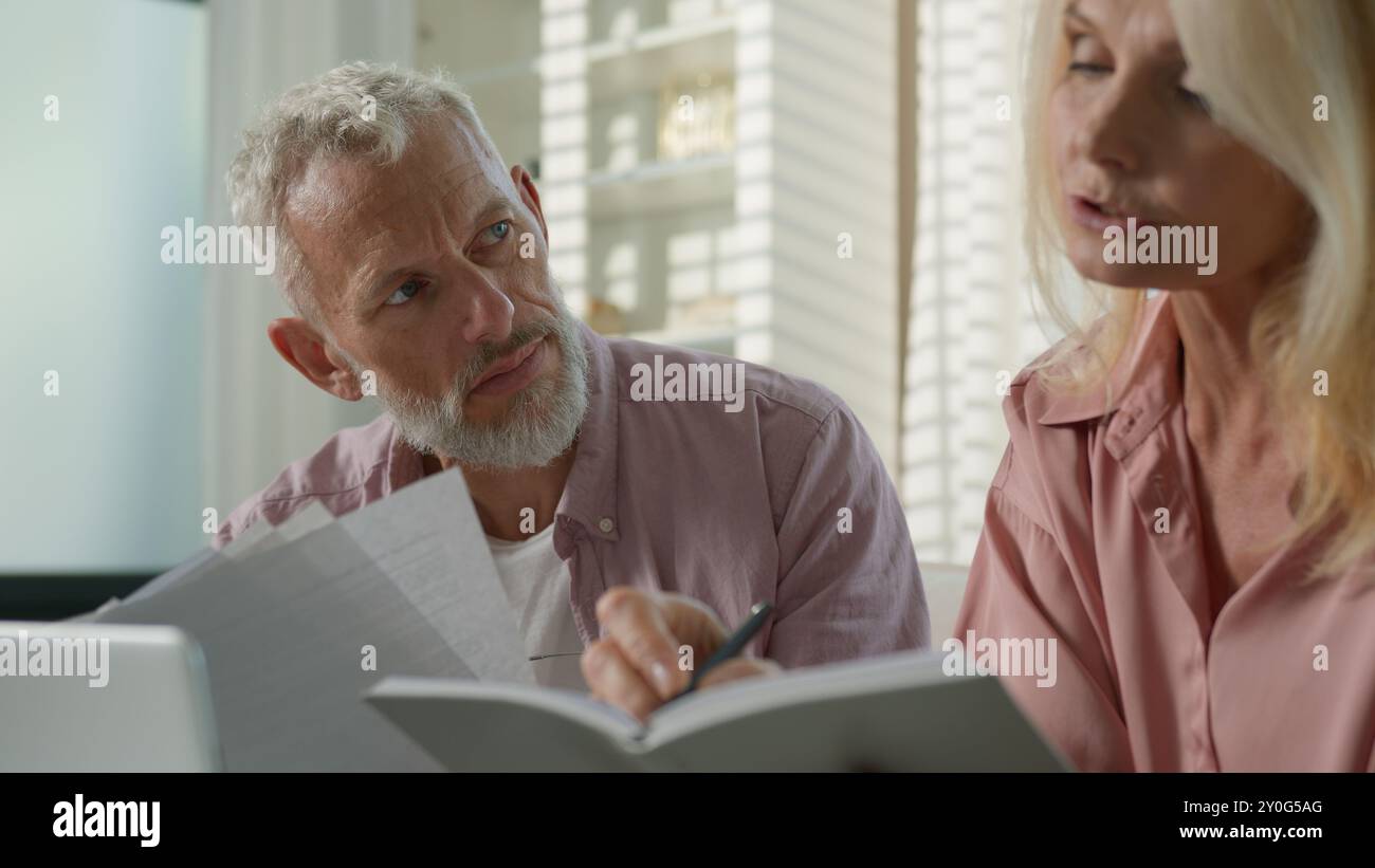 Fatigué pensif couple caucasien famille grands-parents femme mature femme âgée homme âgé retraité masculin parle d'affaires travaillant avec des documents Banque D'Images